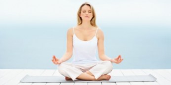 Beautiful young woman sitting in lotus position on dock by the sea