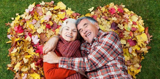 Mature couple laying in autumnal heart shape.